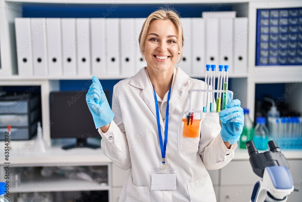Young caucasian woman working at scientist laboratory holding test tubes screaming proud, celebrating victory and success very excited with raised arm
