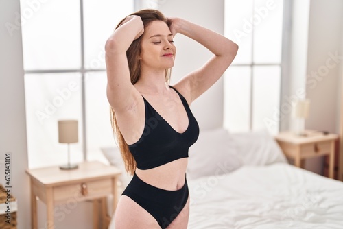 Young caucasian woman smiling confident combing hair with hands at bedroom