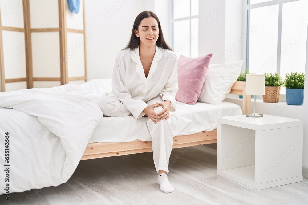 Young hispanic woman suffering for knee pain sitting on bed at bedroom Young hispanic woman suffering for knee pain sitting on bed at bedroom