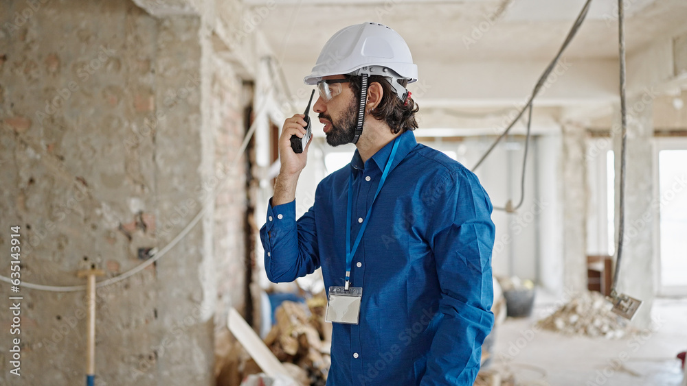 Young hispanic man architect talking on walkie-talkie at construction site