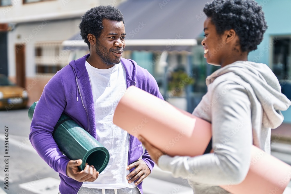 African american man and woman couple holding yoga mat speaking together at street African american man and woman couple holding yoga mat speaking together at street