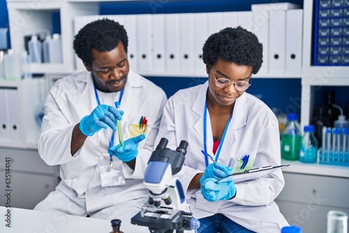 African american man and woman scientists writing on document holding test tube at laboratory