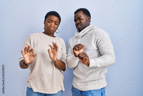 Young african american couple standing over blue background together disgusted expression, displeased and fearful doing disgust face because aversion reaction. photo