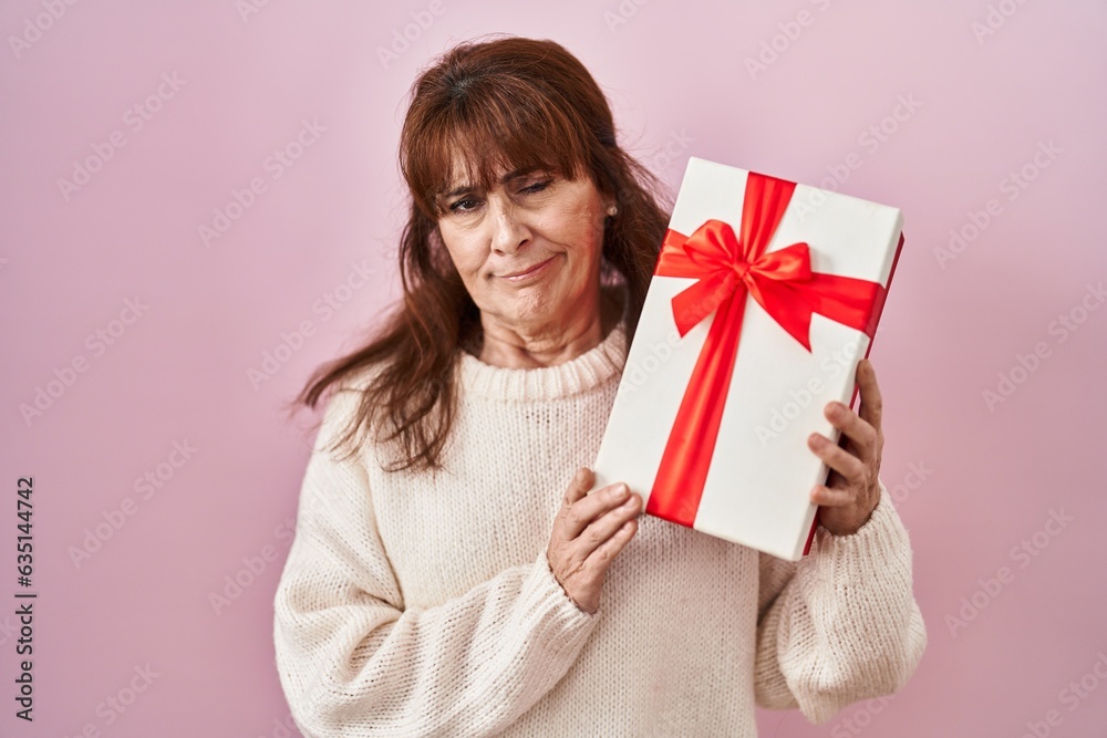 Middle age hispanic woman holding present skeptic and nervous, frowning upset because of problem. negative person. Middle age hispanic woman holding present skeptic and nervous, frowning upset because of problem. negative person.