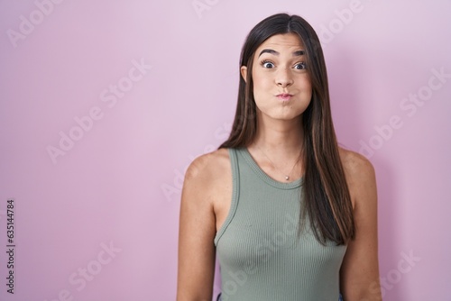 Hispanic woman standing over pink background puffing cheeks with funny face. mouth inflated with air, crazy expression. photo