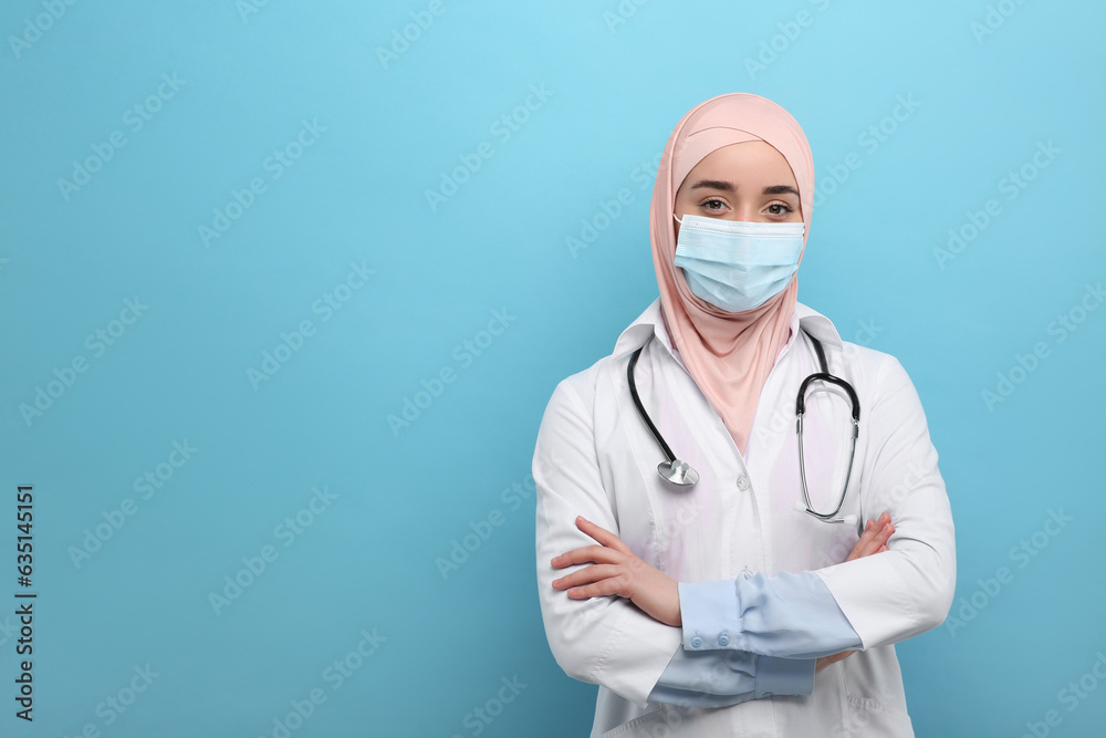 Muslim woman wearing hijab, medical uniform and protective mask on light blue background, space for text Muslim woman wearing hijab, medical uniform and protective mask on light blue background, space for text