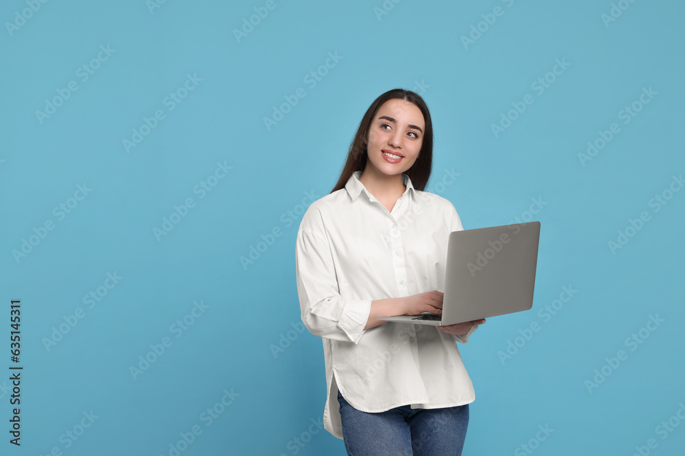 Smiling young woman with laptop on light blue background. Space for text Smiling young woman with laptop on light blue background. Space for text