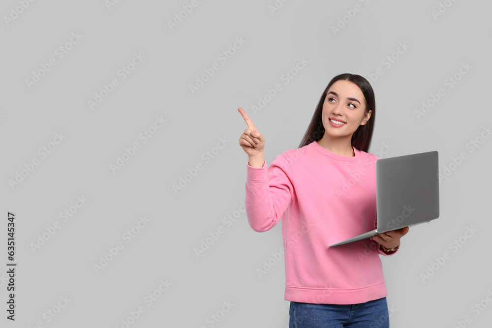 Smiling young woman with laptop on grey background, space for text Smiling young woman with laptop on grey background, space for text