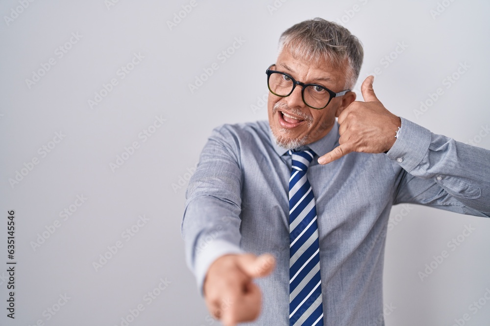 Hispanic business man with grey hair wearing glasses smiling doing talking on the telephone gesture and pointing to you. call me. Hispanic business man with grey hair wearing glasses smiling doing talking on the telephone gesture and pointing to you. call me.