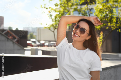 Beautiful smiling woman in sunglasses on city street, space for text