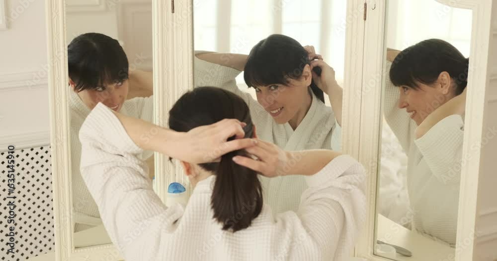 A woman dressed in a comfortable robe sitting by the bedroom mirror, engrossed in creating a stylish hairstyle. Her focused expression and skilled hands work in harmony to craft the perfect look. A woman dressed in a comfortable robe sitting by the bedroom mirror, engrossed in creating a stylish hairstyle. Her focused expression and skilled hands work in harmony to craft the perfect look.