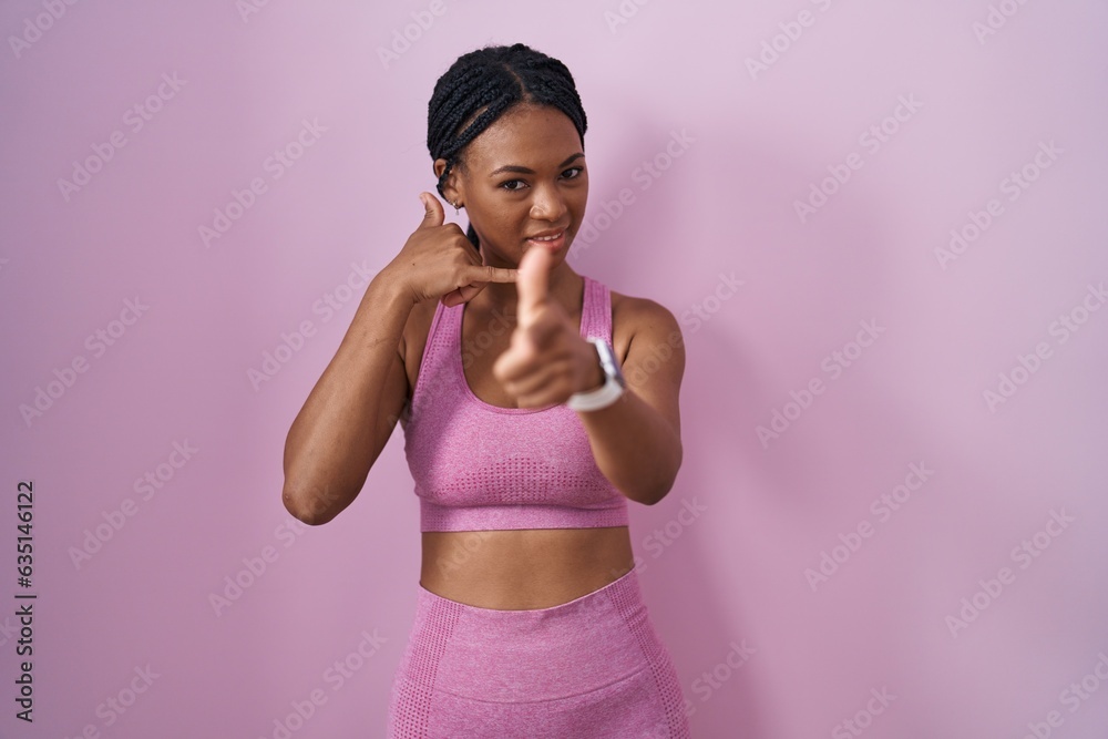 African american woman with braids wearing sportswear over pink background smiling doing talking on the telephone gesture and pointing to you. call me.