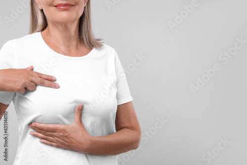 Woman doing breast self-examination on light grey background, closeup. Space for text