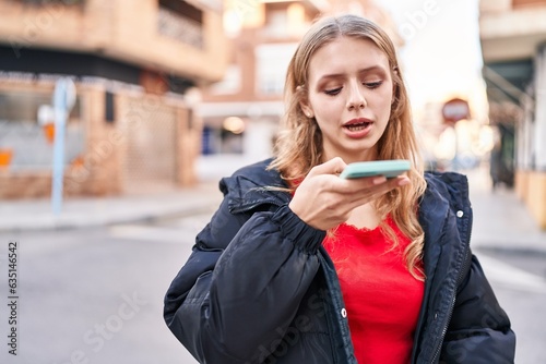 Young blonde woman talking on smartphone with serious expression at street