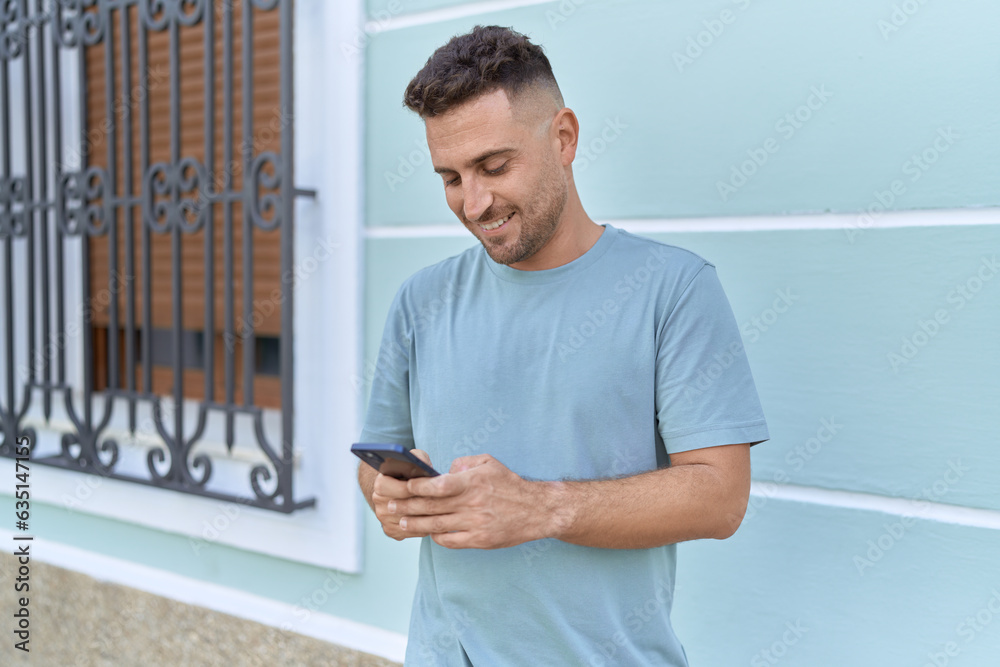 Fototapeta premium Young hispanic man smiling confident using smartphone at street