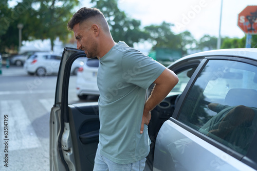 Young hispanic man suffering for backache standing by car at street