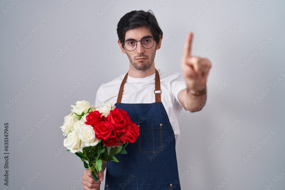 Young hispanic man holding bouquet of white and red roses pointing with finger up and angry expression, showing no gesture Young hispanic man holding bouquet of white and red roses pointing with finger up and angry expression, showing no gesture