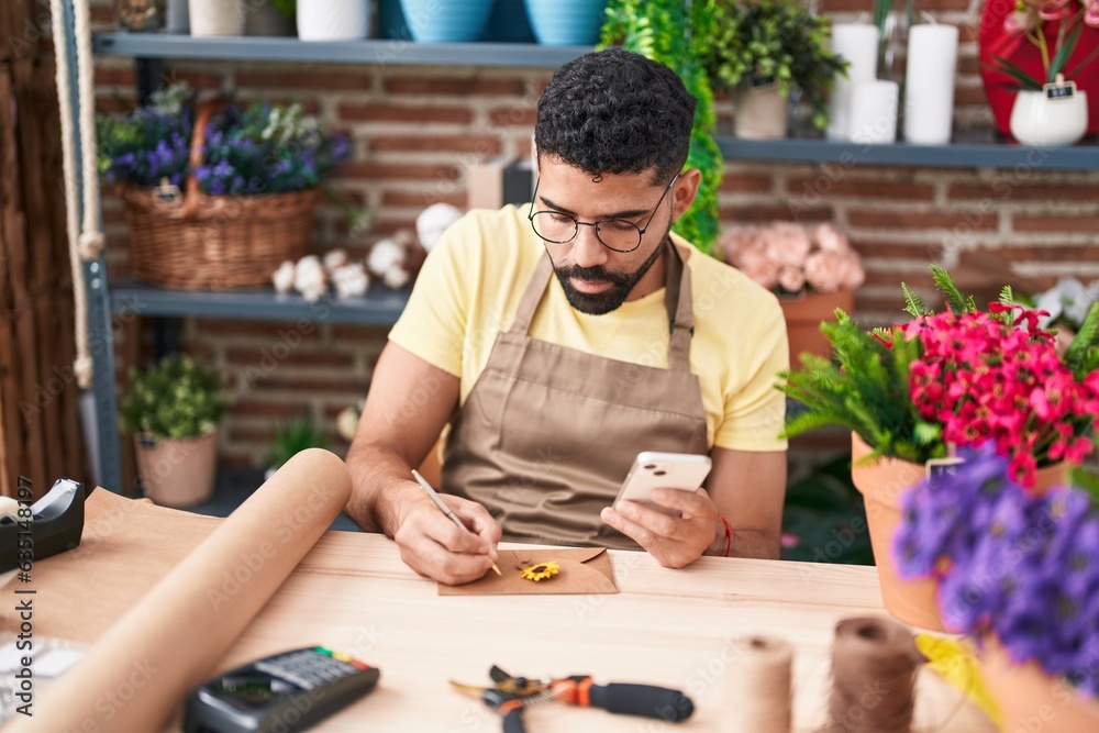 Young arab man florist writing on envelope letter using smartphone at florist Young arab man florist writing on envelope letter using smartphone at florist