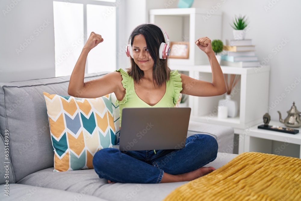 Hispanic young woman using laptop at home showing arms muscles smiling proud. fitness concept. Hispanic young woman using laptop at home showing arms muscles smiling proud. fitness concept.