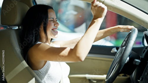Young beautiful hispanic woman driving a car dancing with the music at street