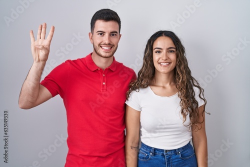 Young hispanic couple standing over isolated background showing and pointing up with fingers number four while smiling confident and happy.