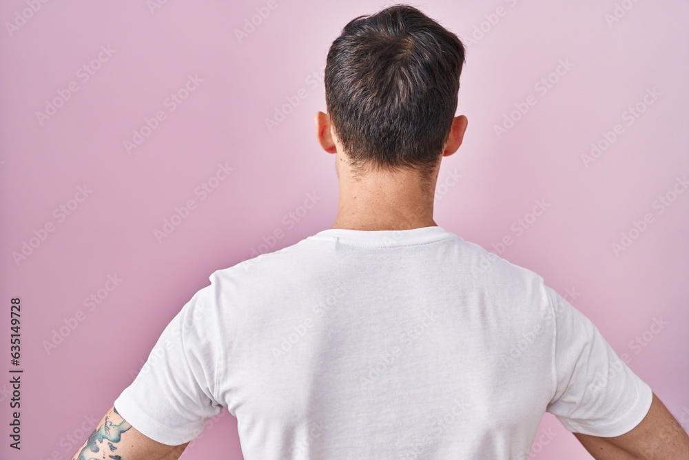 Caucasian man standing over pink background standing backwards looking away with arms on body Caucasian man standing over pink background standing backwards looking away with arms on body