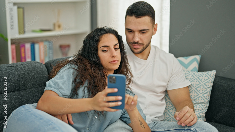 Man and woman couple using smartphone sitting on sofa at home Man and woman couple using smartphone sitting on sofa at home