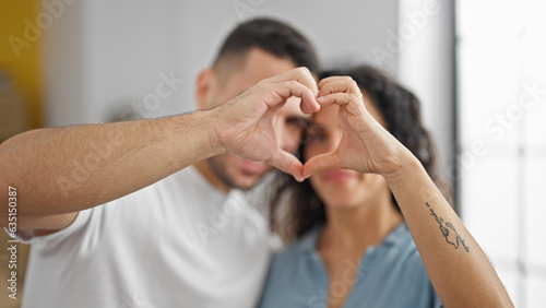 Man and woman couple standing together doing heart gesture at new home