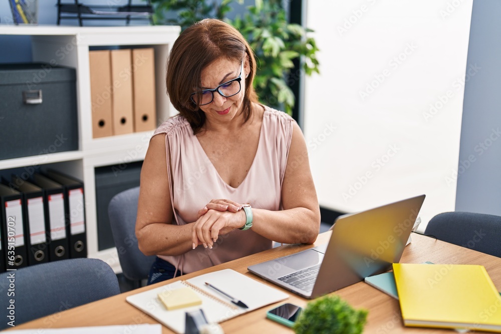 Middle age woman business worker using laptop looking watch at office Middle age woman business worker using laptop looking watch at office