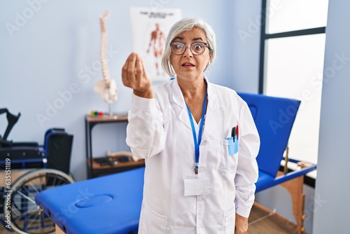 Middle age woman with grey hair working at pain recovery clinic doing italian gesture with hand and fingers confident expression