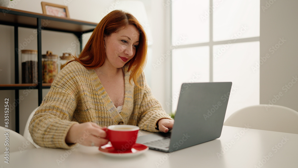 Young redhead woman using laptop drinking coffee at home Young redhead woman using laptop drinking coffee at home