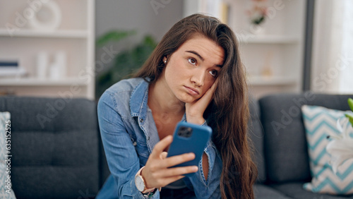 Young beautiful hispanic woman using smartphone sitting on sofa with sad expression at home