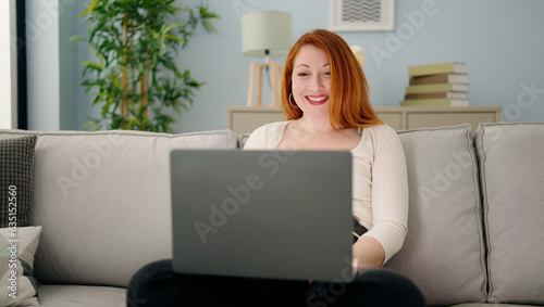 Young redhead woman using laptop sitting on sofa at home