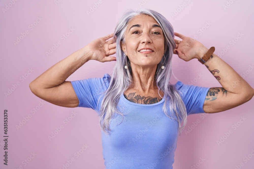 Middle age woman with tattoos standing over pink background smiling pulling ears with fingers, funny gesture. audition problem Middle age woman with tattoos standing over pink background smiling pulling ears with fingers, funny gesture. audition problem