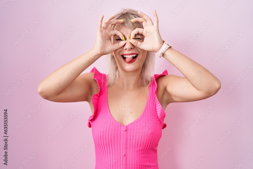 Φωτογραφία Young caucasian woman standing over pink background doing ok gesture like binoculars sticking tongue out, eyes looking through fingers