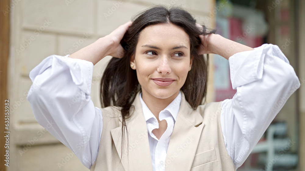 Young beautiful hispanic woman smiling confident combing hair with hands at street Young beautiful hispanic woman smiling confident combing hair with hands at street