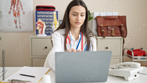 Young beautiful hispanic woman doctor using laptop working at clinic