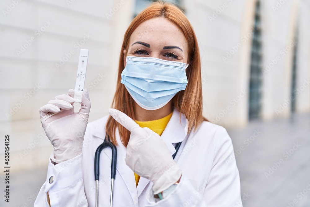 Young doctor woman holding coronavirus infection test smiling happy pointing with hand and finger Young doctor woman holding coronavirus infection test smiling happy pointing with hand and finger