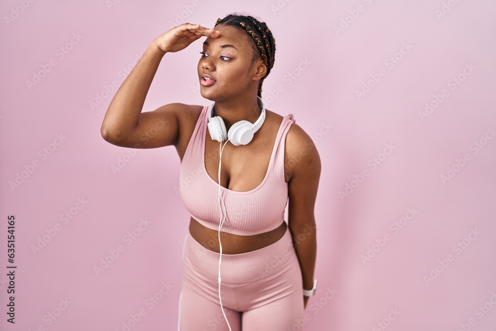 African american woman with braids wearing sportswear and headphones very happy and smiling looking far away with hand over head. searching concept.