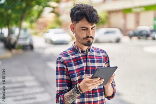 Young hispanic man using touchpad standing at street