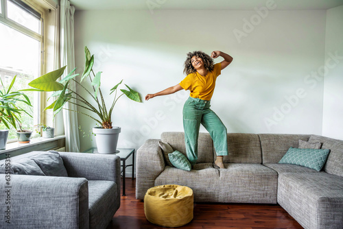 Fototapeta Naklejka Na Ścianę i Meble -  Happy afro american woman dancing on the sofa at home - Smiling girl enjoying day off lying on the couch - Healthy life style, good vibes people and new home concept