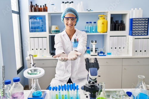 Brunette woman working at scientist laboratory smiling with hands palms together receiving or giving gesture. hold and protection