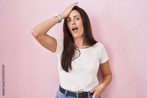 Foto Young brunette woman standing over pink background surprised with hand on head for mistake, remember error