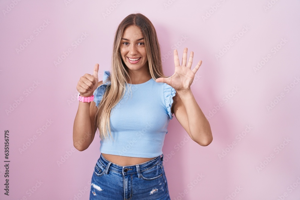 Young blonde woman standing over pink background showing and pointing up with fingers number six while smiling confident and happy. Young blonde woman standing over pink background showing and pointing up with fingers number six while smiling confident and happy.