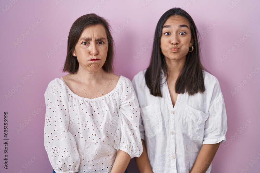 Hispanic mother and daughter together puffing cheeks with funny face. mouth inflated with air, crazy expression. Hispanic mother and daughter together puffing cheeks with funny face. mouth inflated with air, crazy expression.