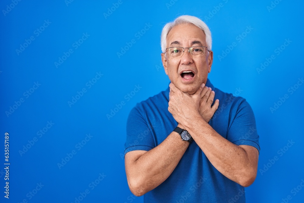 Middle age man with grey hair standing over blue background shouting and suffocate because painful strangle. health problem. asphyxiate and suicide concept. Middle age man with grey hair standing over blue background shouting and suffocate because painful strangle. health problem. asphyxiate and suicide concept.