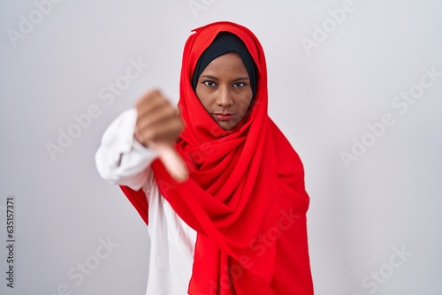 Young arab woman wearing traditional islamic hijab scarf looking unhappy and angry showing rejection and negative with thumbs down gesture. bad expression.