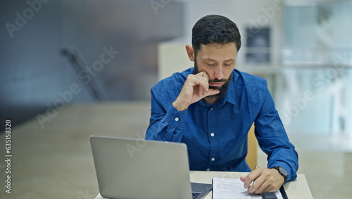 Young hispanic man business worker using laptop taking notes at the office