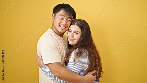 Man and woman couple smiling confident hugging each other over isolated yellow background