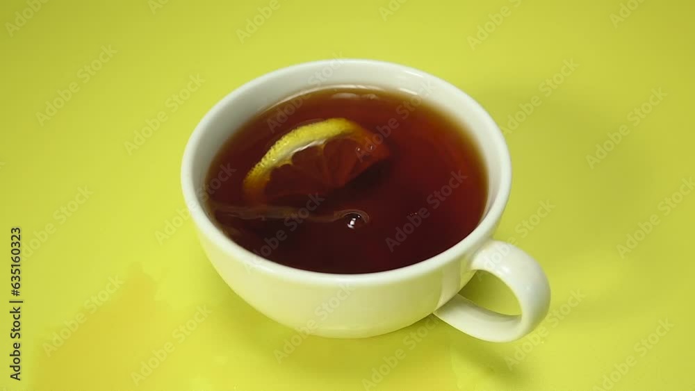 Putting lemon into black tea top view. White cup of tea on yellow background, top view, slow motion Putting lemon into black tea top view. White cup of tea on yellow background, top view, slow motion